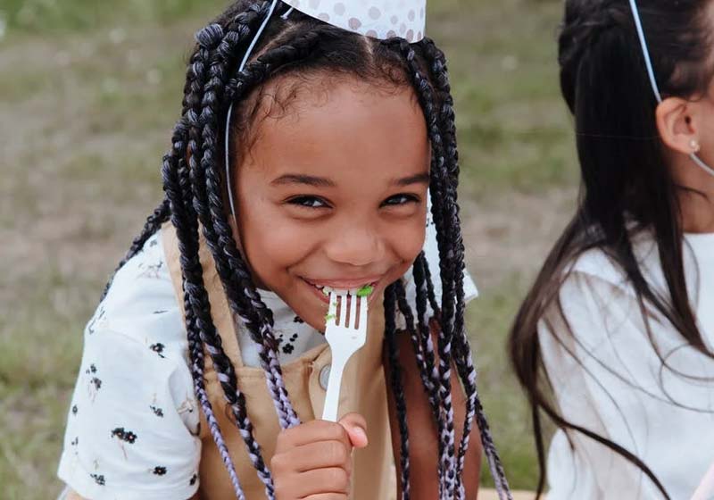 menina sorrindo comendo bolo em festa de aniversario infantil