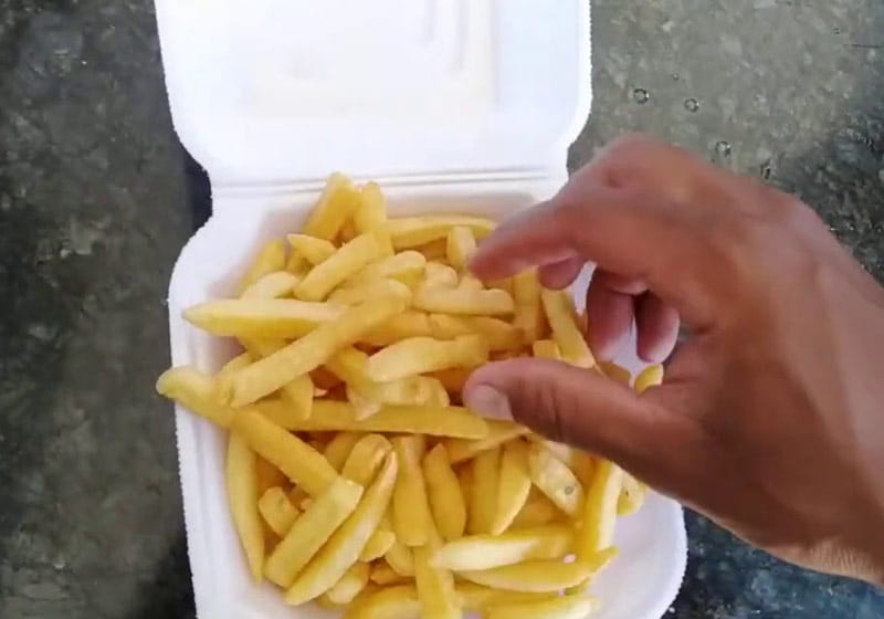 uma mão pegando a batata dentro de uma embalagem de isopor com batatas fritas