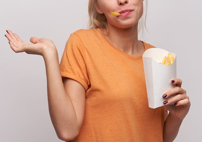 uma mulher segurando uma embalagem de fritas com uma batata na boca